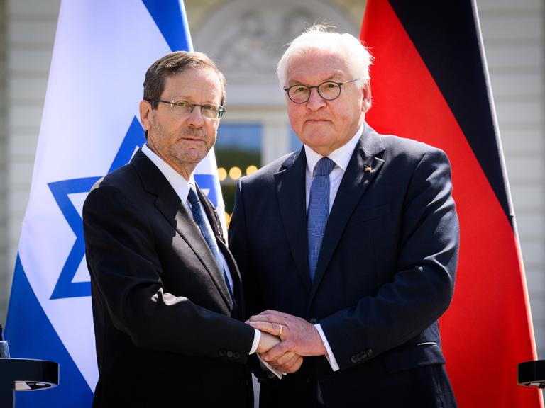 Bundespräsident Frank-Walter Steinmeier (r) und Izchak Herzog, Präsident von Israel, geben sich am Ende einer Pressekonferenz nach ihrem Gespräch im Schloss Bellevue die Hand. Im Hintergrund die Fahnen beider Staaten. 