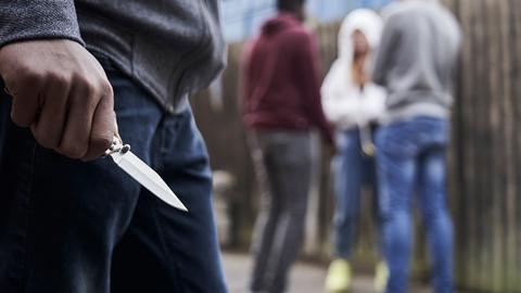 Jugendlicher hält ein Messer in der Hand, im Hintergrund stehen andere Jugendliche