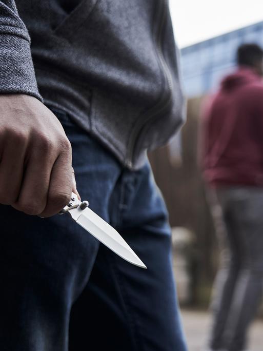Jugendlicher hält ein Messer in der Hand, im Hintergrund stehen andere Jugendliche