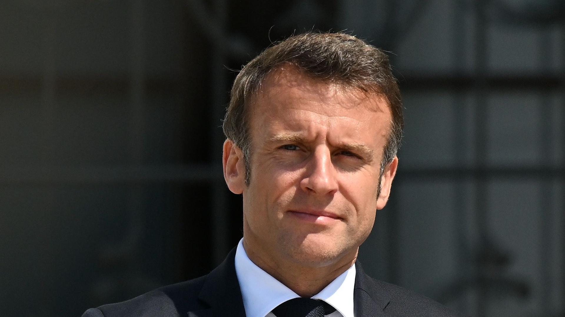 Macron in einer Portraitaufnahme im Anzug. Ihm scheint die Sonne ins Gesicht.