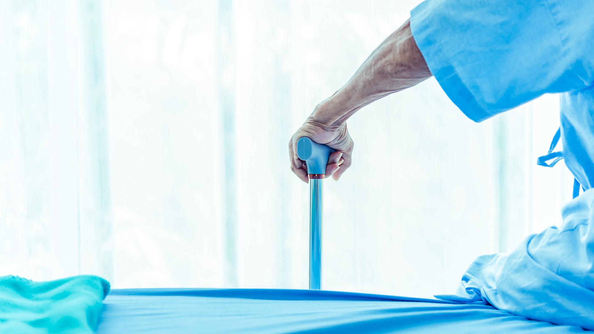Ein Mensch in blauer Krankenhausbekleidung stützt sich auf einen blauen Gehstock.