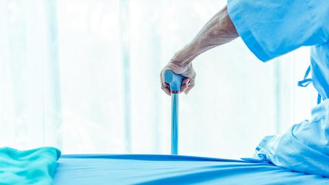 Ein Mensch in blauer Krankenhausbekleidung stützt sich auf einen blauen Gehstock.