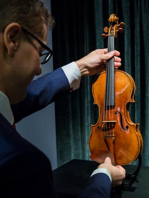 Ein Mann hält eine Geige in den Händen und betrachtet das Instrument