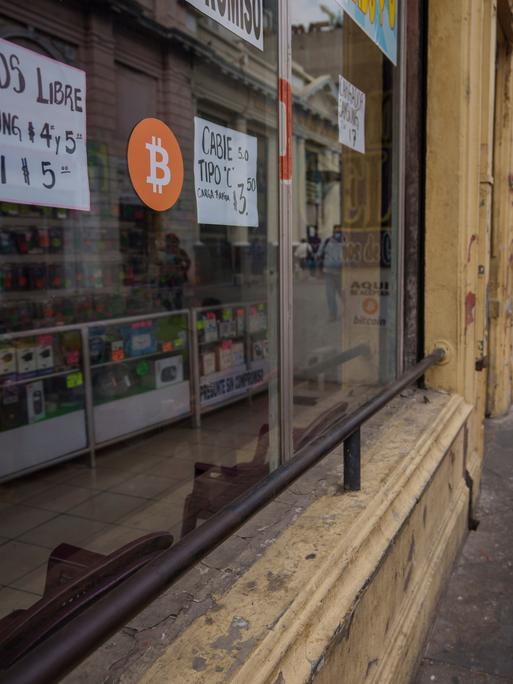 Ein Zeichen für die Zahlungsmöglichkeit mit Bitcoin ist an der Fensterscheibe eines kleinen Straßengeschäfts angebracht. 