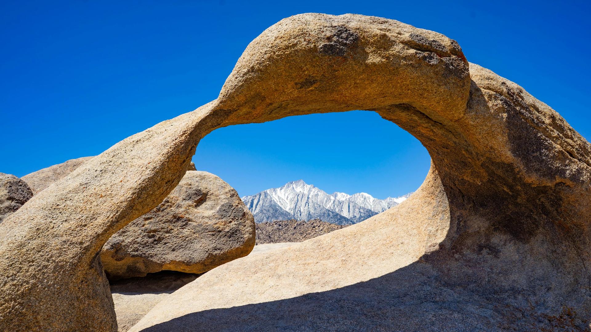 Ein Felsbogen in einer Wüstenlandschaft, der den Blick auf Hochgebirge freigibt. Ein Felsbogen in einer Wüstenlandschaft, der den Blick auf Hochgebirge freigibt.