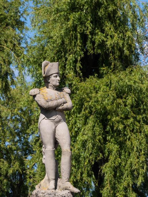 Ein steinernes Monument zeigt Napoleon mit verschränkten Armen in Uniform, während er seine Arme verschränkt.
