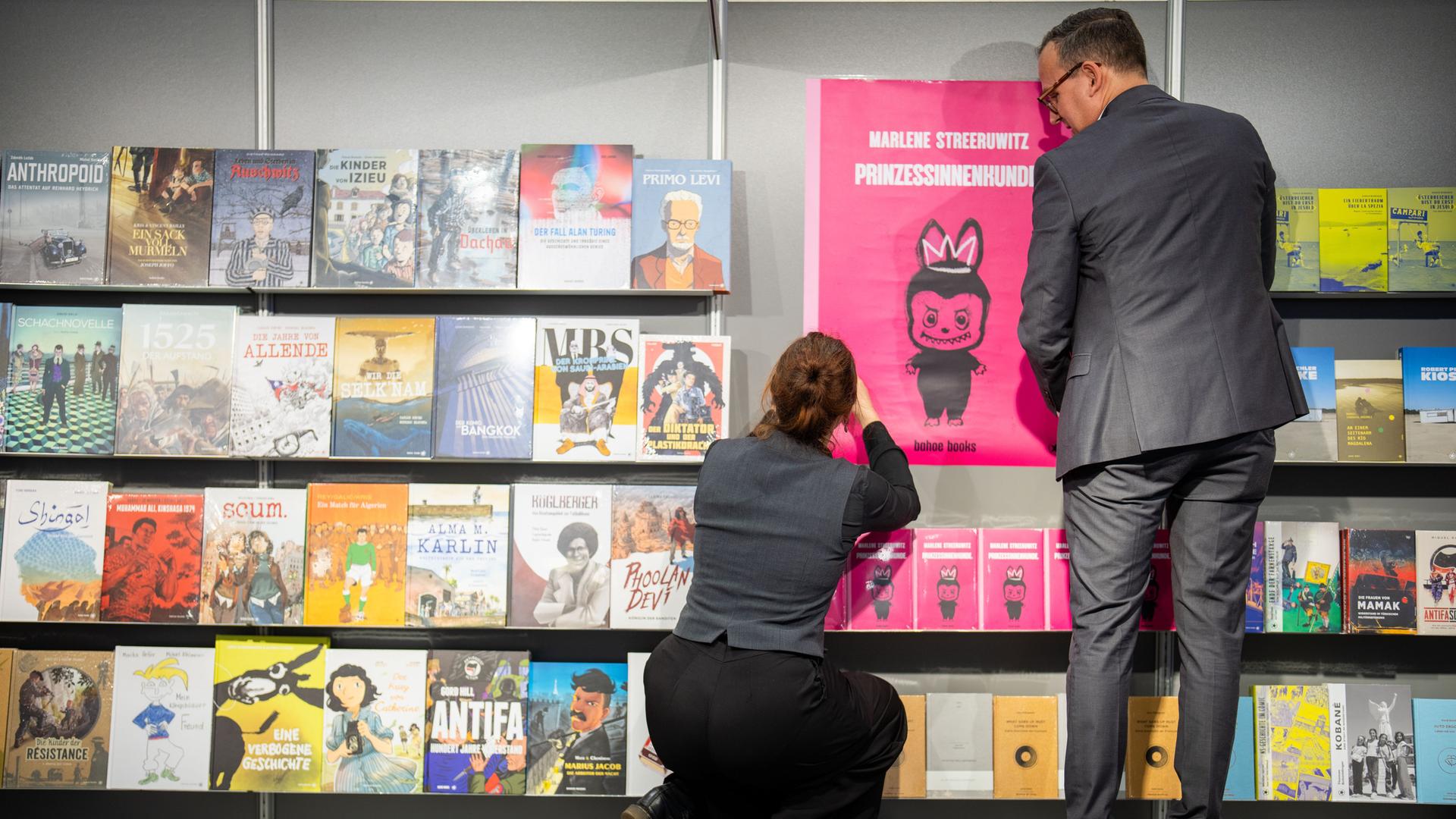 Ein Mann und eine Frau stehen bei der Messe "Buch Wien" vor einem Bücherregal. 