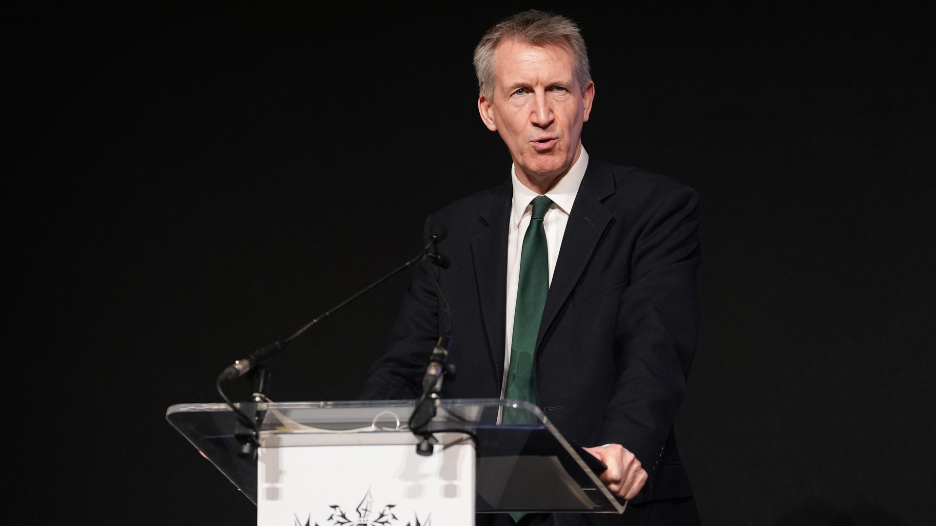Dan Jarvis steht an einem Pult und spricht. Der Bildhintergrund ist schwarz. Dan Jarvis steht an einem Pult und spricht. Der Bildhintergrund ist schwarz.