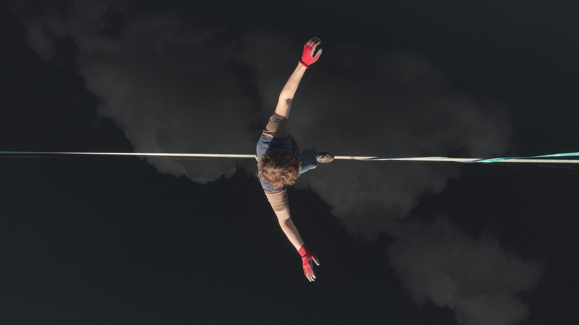 Ein Seiltänzer von (oben fotografiert) läuft auf einem Seil über Wolken. 
