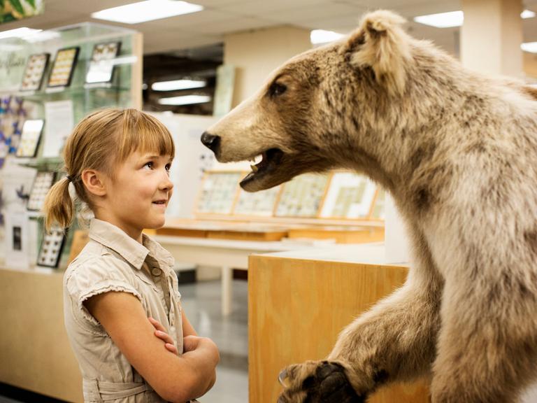 Ein Mädchen steht einem ausgestopften Bär im Museum gegenüber