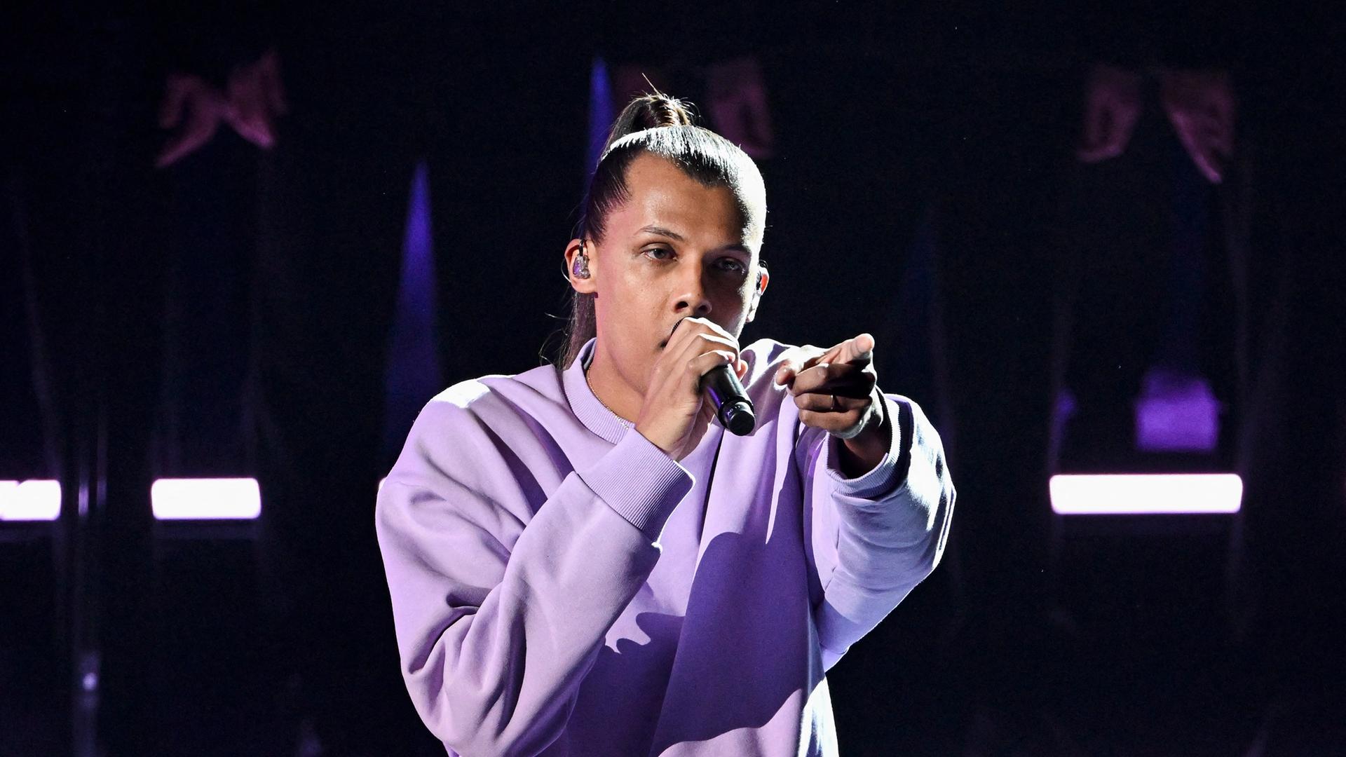 Stromae bei einem Konzert in Boulogne-Billancourt mit lila Pulli und Mikrophon in der Hand. Stromae bei einem Konzert in Boulogne-Billancourt mit lila Pulli und Mikrophon in der Hand.