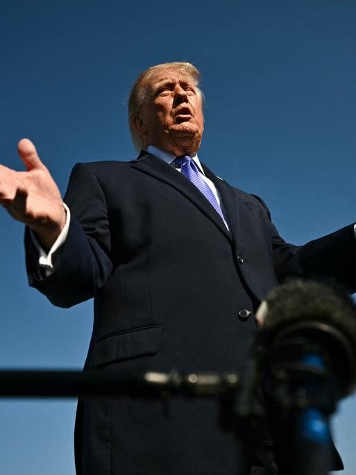 Starke Untersicht auf Donald Trump, der gestikulierend in ein Mikrofon spricht.