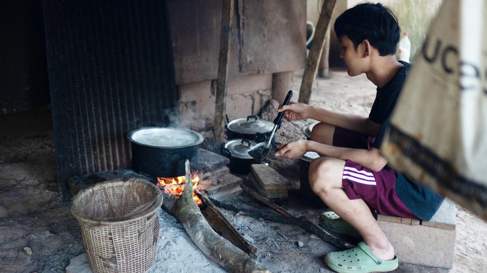 Ein Junge, der mit seiner Familie vor den Angriffen der Militärjunta geflohen ist, kocht Reis in einem Vertriebenencamp im Dschungel an der Grenze zu Thailand. Sauberes Trinkwasser gibt es nicht, Lebensmittel sind knapp. 16.01.2023.