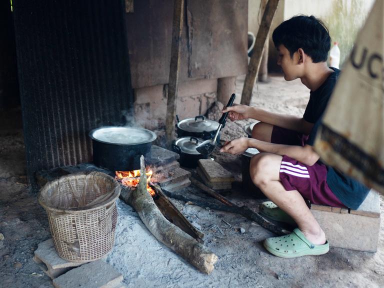 Ein Junge, der mit seiner Familie vor den Angriffen der Militärjunta geflohen ist, kocht Reis in einem Vertriebenencamp im Dschungel an der Grenze zu Thailand. Sauberes Trinkwasser gibt es nicht, Lebensmittel sind knapp. 16.01.2023.