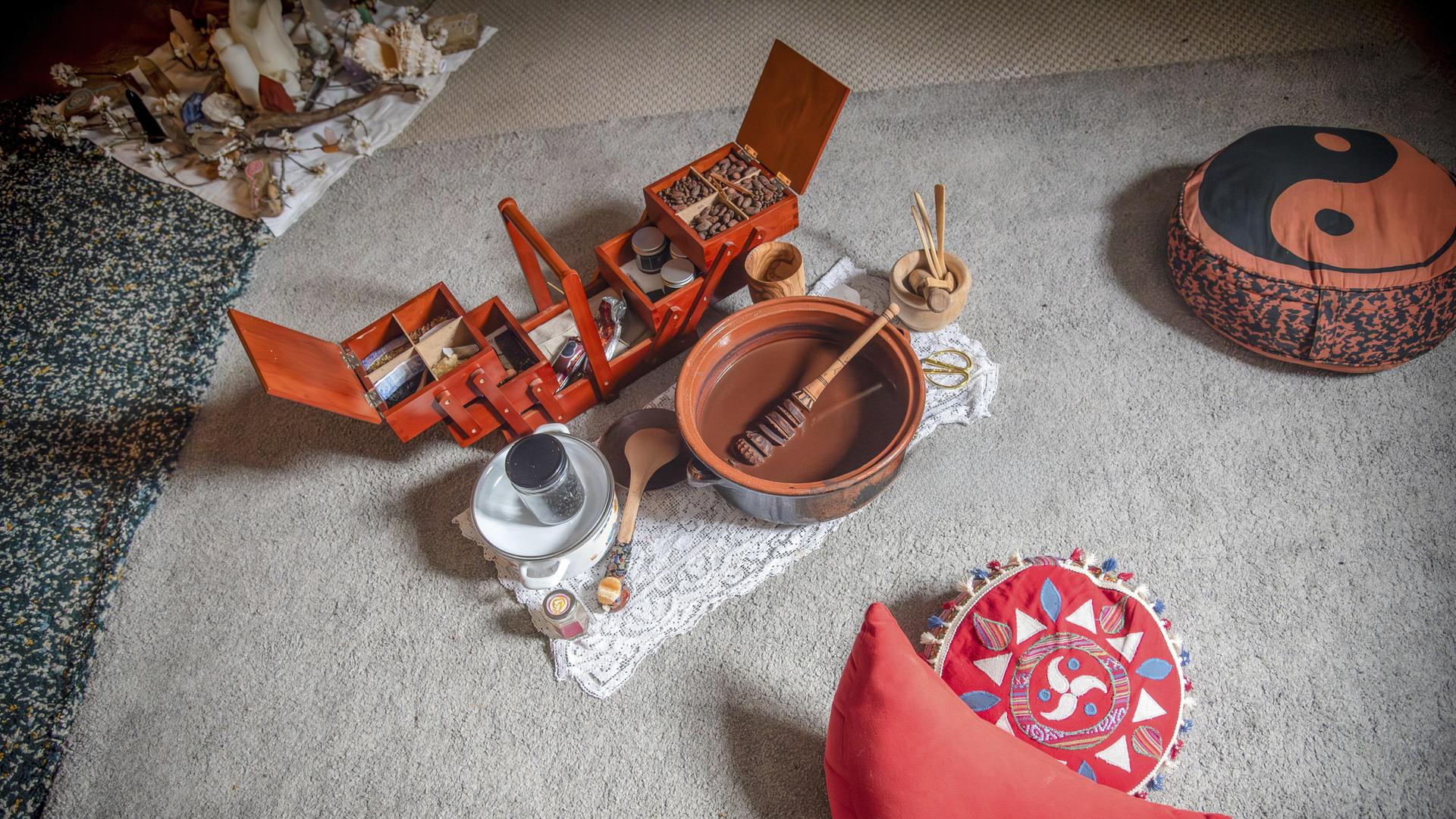 Meditationsecke mit roten Sitzkissen und einem Set aus Holzboxen, Schalen und Utensilien auf einem Teppich