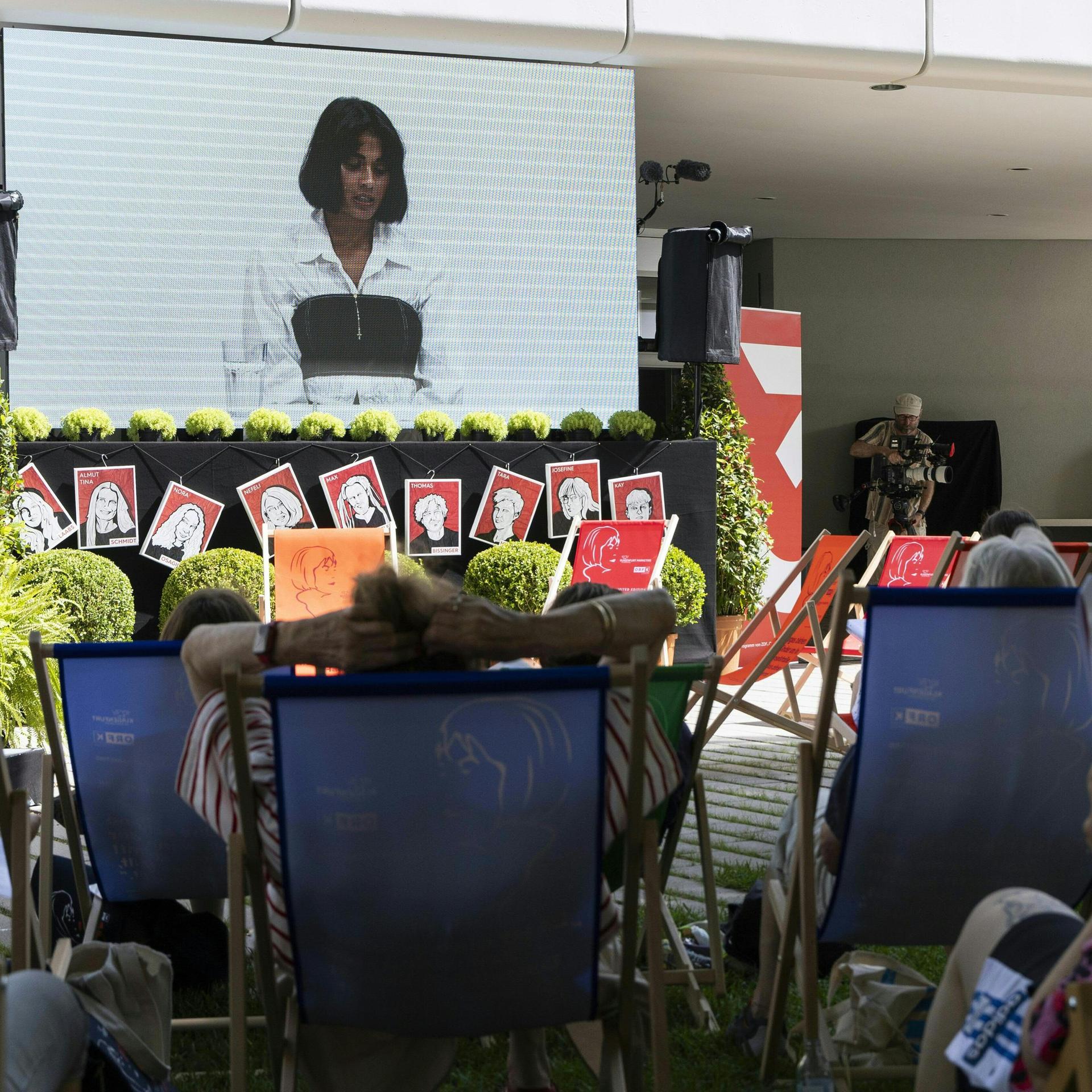 Menschen liegen in Liegestühlen vor einer Leinwand, aber der eine Lesung beim Ingeborg-Bachmann-Preis übertragen wird.