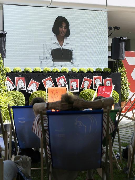 Menschen liegen in Liegestühlen vor einer Leinwand, aber der eine Lesung beim Ingeborg-Bachmann-Preis übertragen wird.