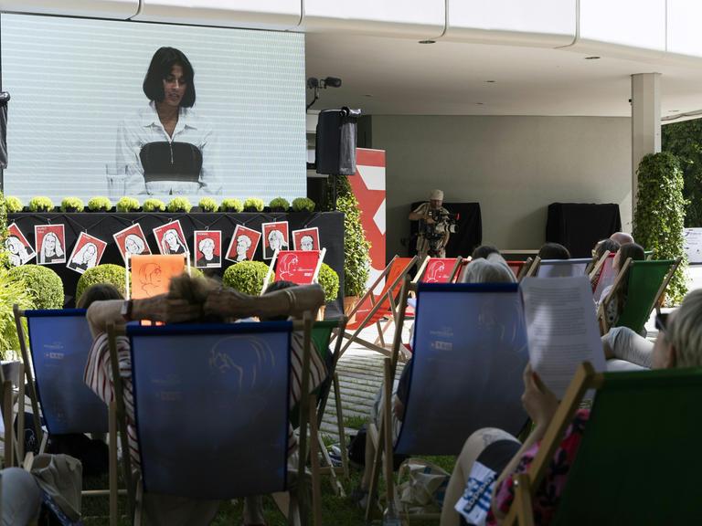 Menschen liegen in Liegestühlen vor einer Leinwand, aber der eine Lesung beim Ingeborg-Bachmann-Preis übertragen wird.
