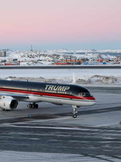 Ein Flugzeug mit dem Schriftzug "Trump" landet auf dem Flughafen von Nuuk. Im Hintergrund sind die verschneite Stadt und der Fjord zu sehen.