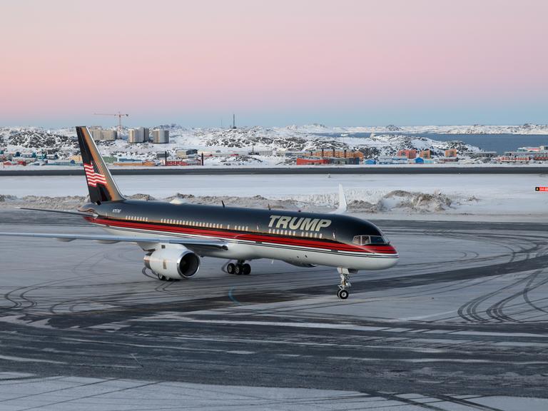 Ein Flugzeug mit dem Schriftzug "Trump" landet auf dem Flughafen von Nuuk. Im Hintergrund sind die verschneite Stadt und der Fjord zu sehen.