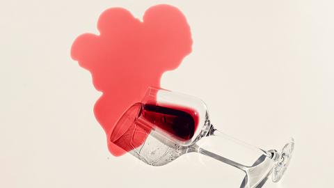 Rotwein rinnt aus einem Weinglas auf einen hellen Untergrund und hinterlässt einen Fleck