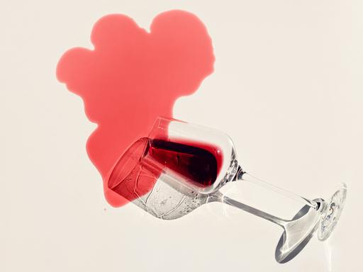 Rotwein rinnt aus einem Weinglas auf einen hellen Untergrund und hinterlässt einen Fleck Rotwein rinnt aus einem Weinglas auf einen hellen Untergrund und hinterlässt einen Fleck