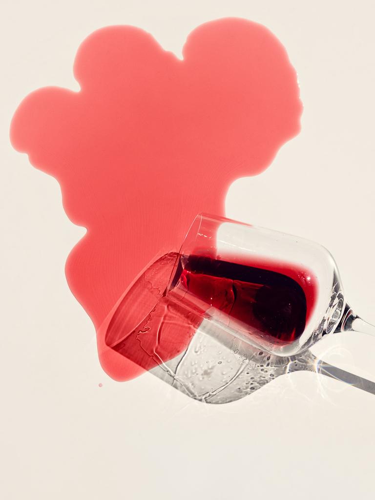 Rotwein rinnt aus einem Weinglas auf einen hellen Untergrund und hinterlässt einen Fleck Rotwein rinnt aus einem Weinglas auf einen hellen Untergrund und hinterlässt einen Fleck