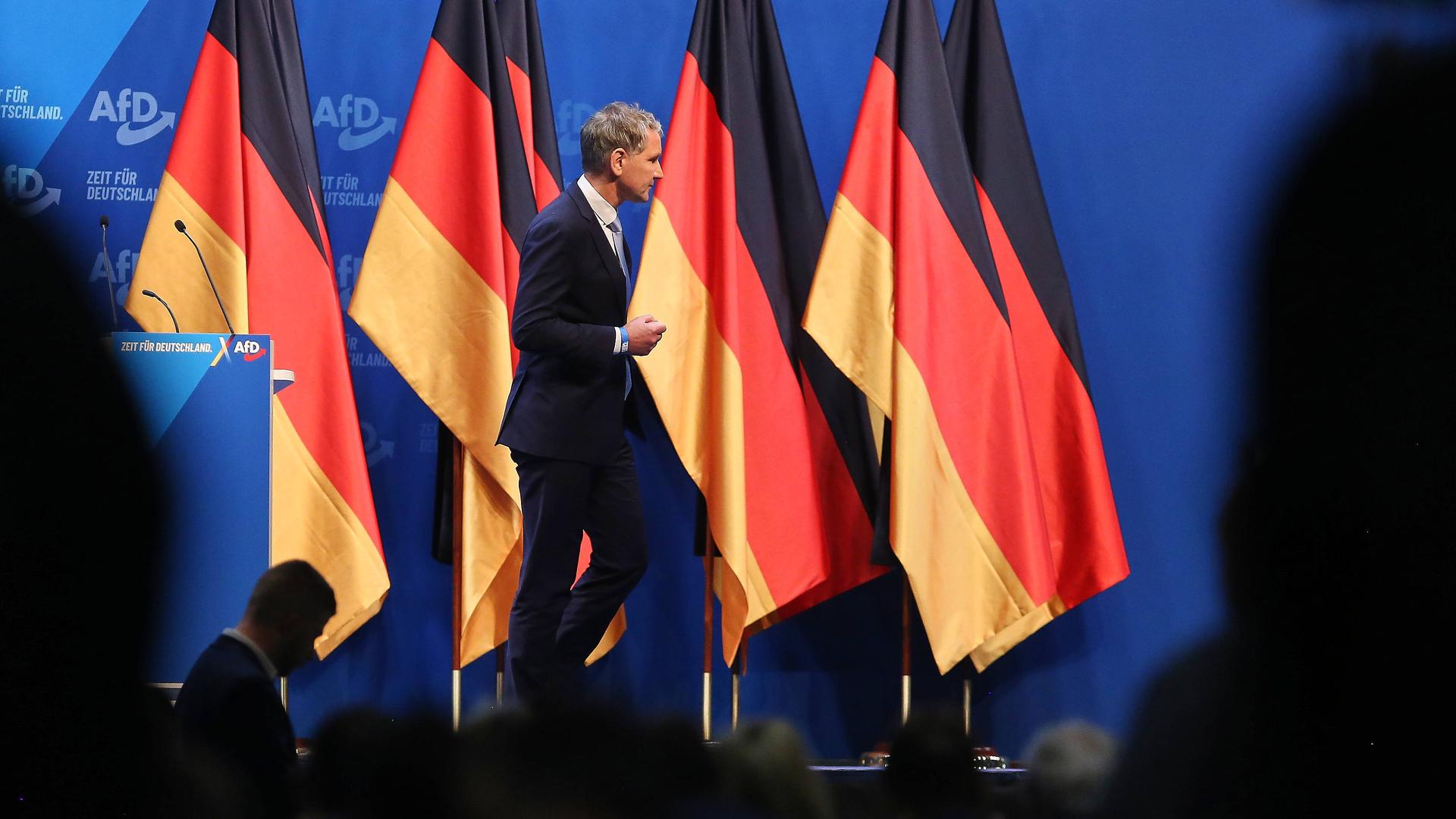 Björn Höcke läuft auf einer Bühne an aneinander aufgereihten Deutschlandflaggen vorbei.