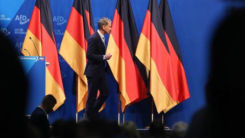 Björn Höcke läuft auf einer Bühne an aneinander aufgereihten Deutschlandflaggen vorbei.