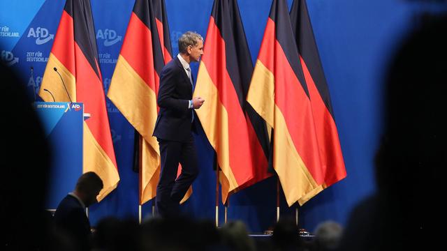 Björn Höcke läuft auf einer Bühne an aneinander aufgereihten Deutschlandflaggen vorbei.