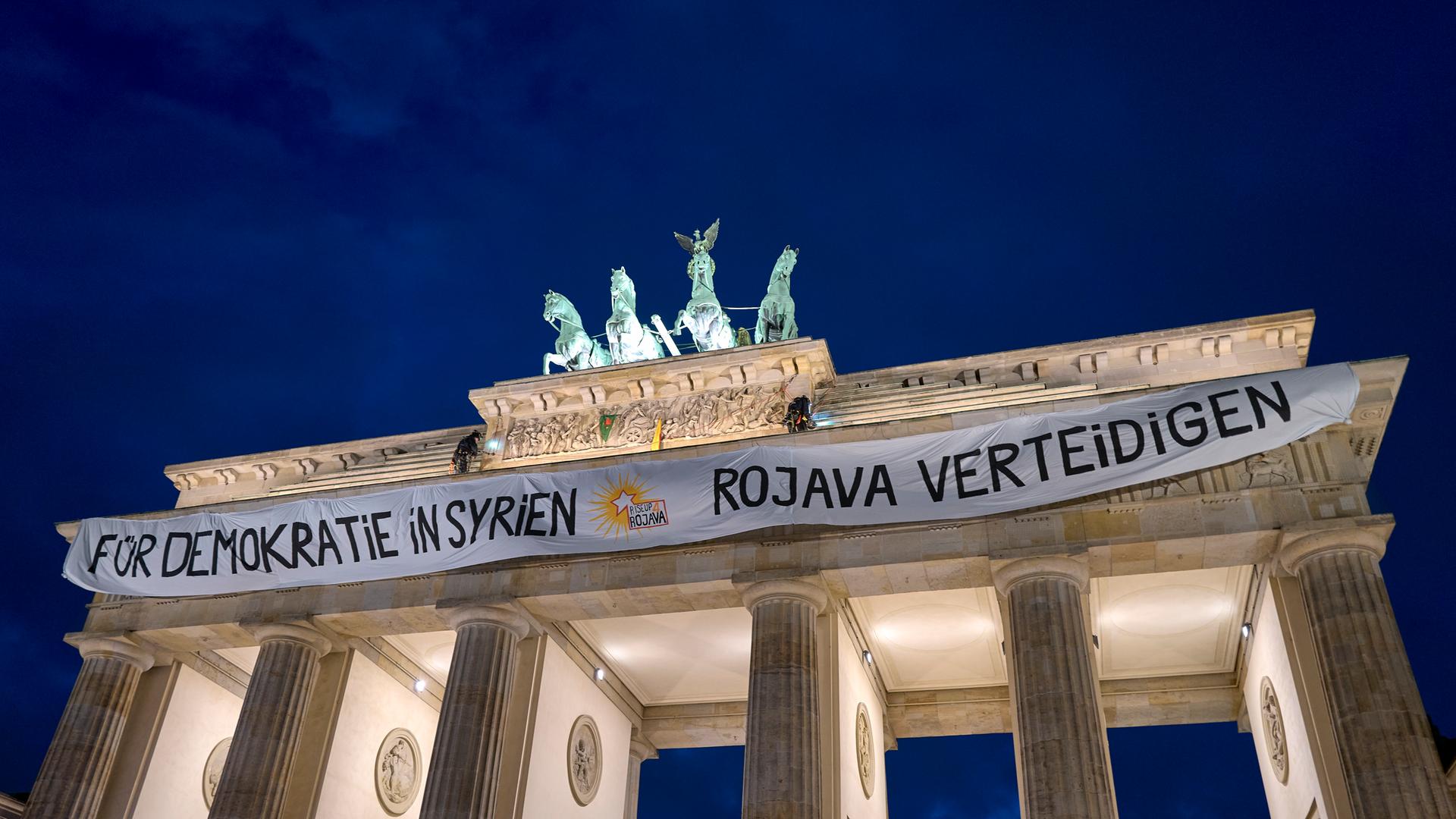 Aktivisten entrollen auf dem Brandenburger Tor ein Transparent mit der Aufschrift Â«Für Demokratie in Syrien - Rojava verteidigenÂ» als Symbol der Solidarität mit den kurdischen Gebieten in Syrien.