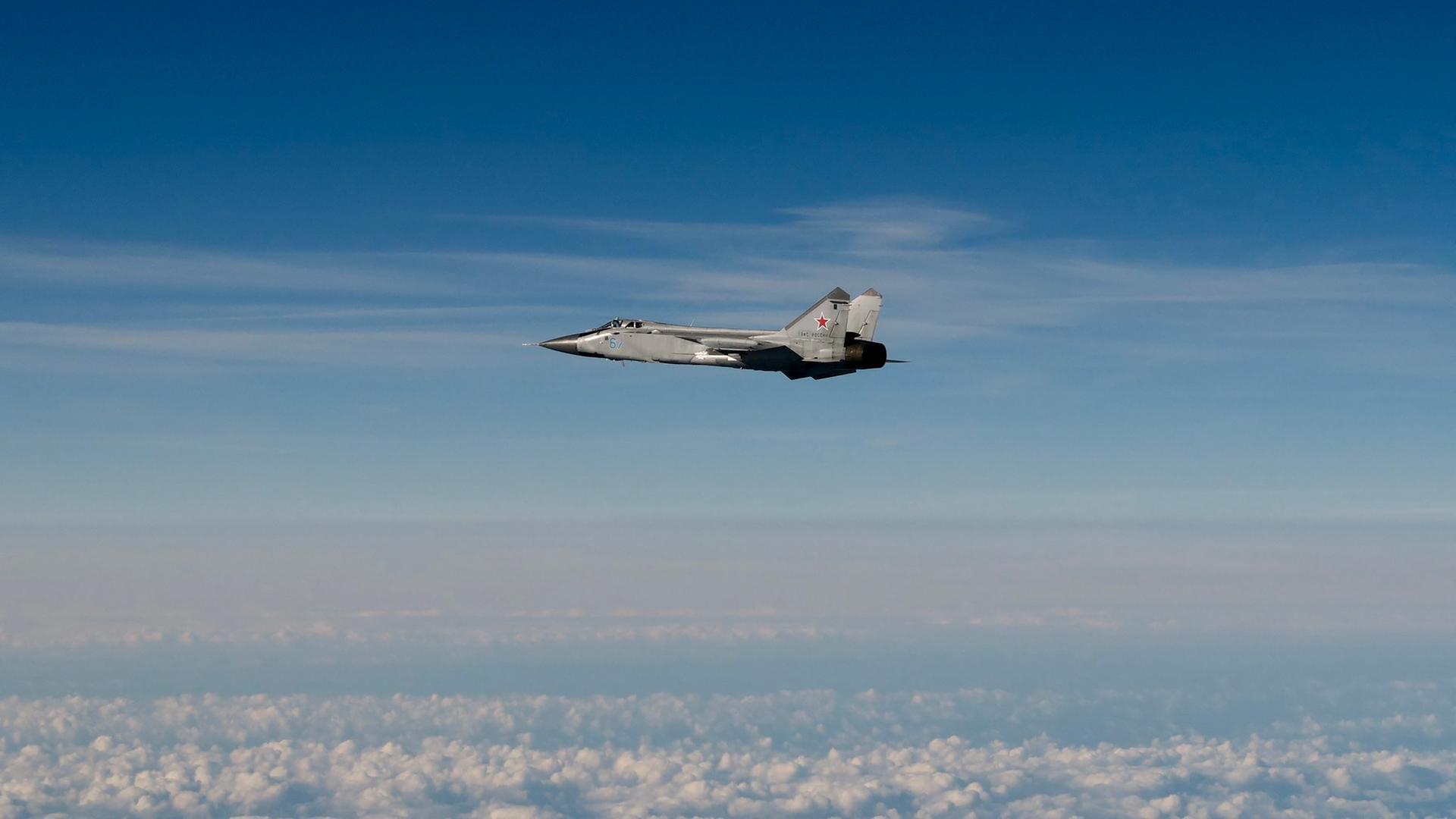 Blick aus großer Ferne auf den Kampfjet unter teils bewölktem Himmel.