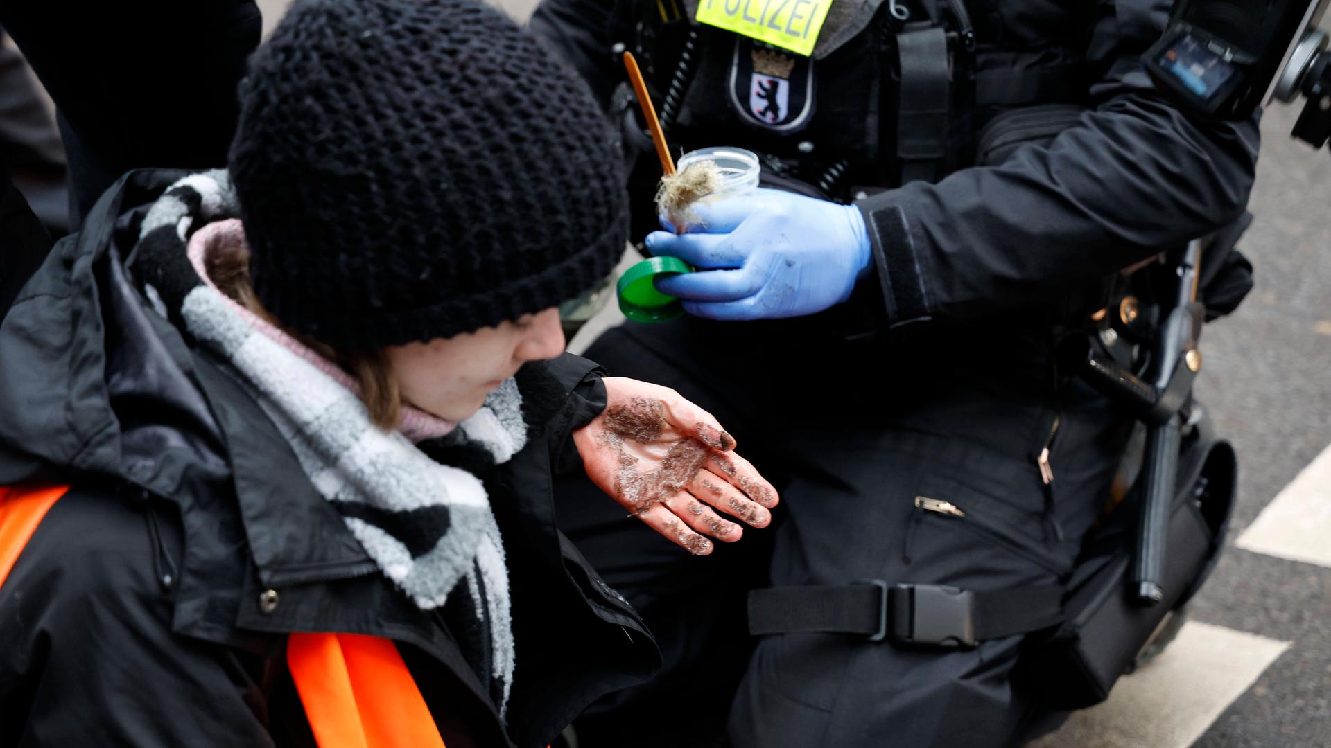 Eine junge Aktivistin der Letzten Generation hat sich in Berlin auf einer Straße festgeklebt, ihre Hände zeigen die Sekundenkleberspuren, nachdem ein Polizist sie losgemacht hat.