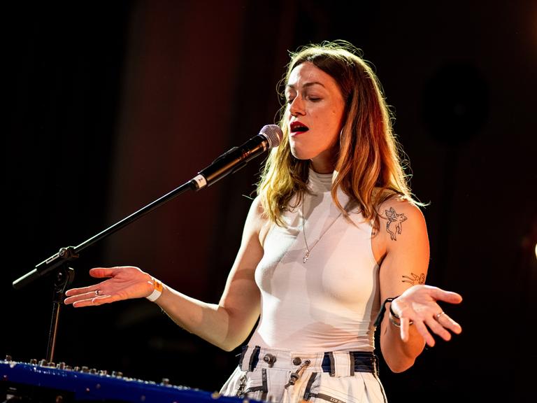 Die Musikerin Charlotte Brandi. Eine junge Frau steht auf einer Bühne und singt in ein Mikrofon.