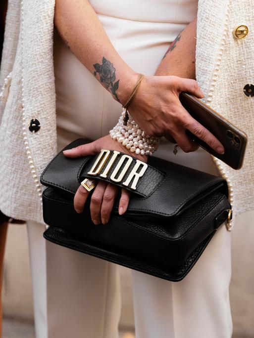 Frauenhand mit Perlenkette umfasst eine Handtasche mit der Aufschrift Dior 