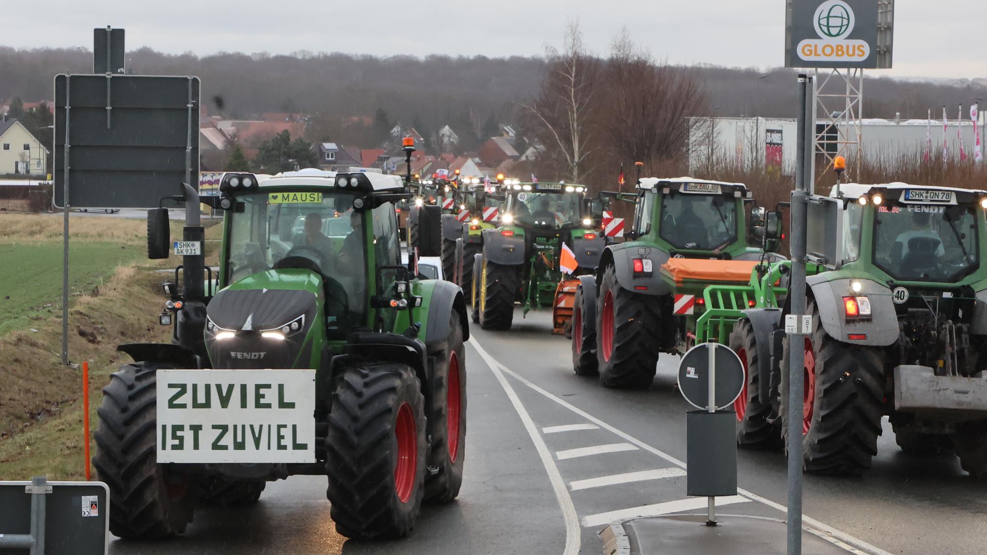 Bauernprotest in Thüringen gegen die Agrarpolitik der Ampelregierung. Zu sehen sind mehrere Traktoren auf einer Straße, die vermutlich nach Berlin fahren. An einem hängt ein Schild, das bemalt ist mit dem Slogan "Zuviel ist zu viel". 