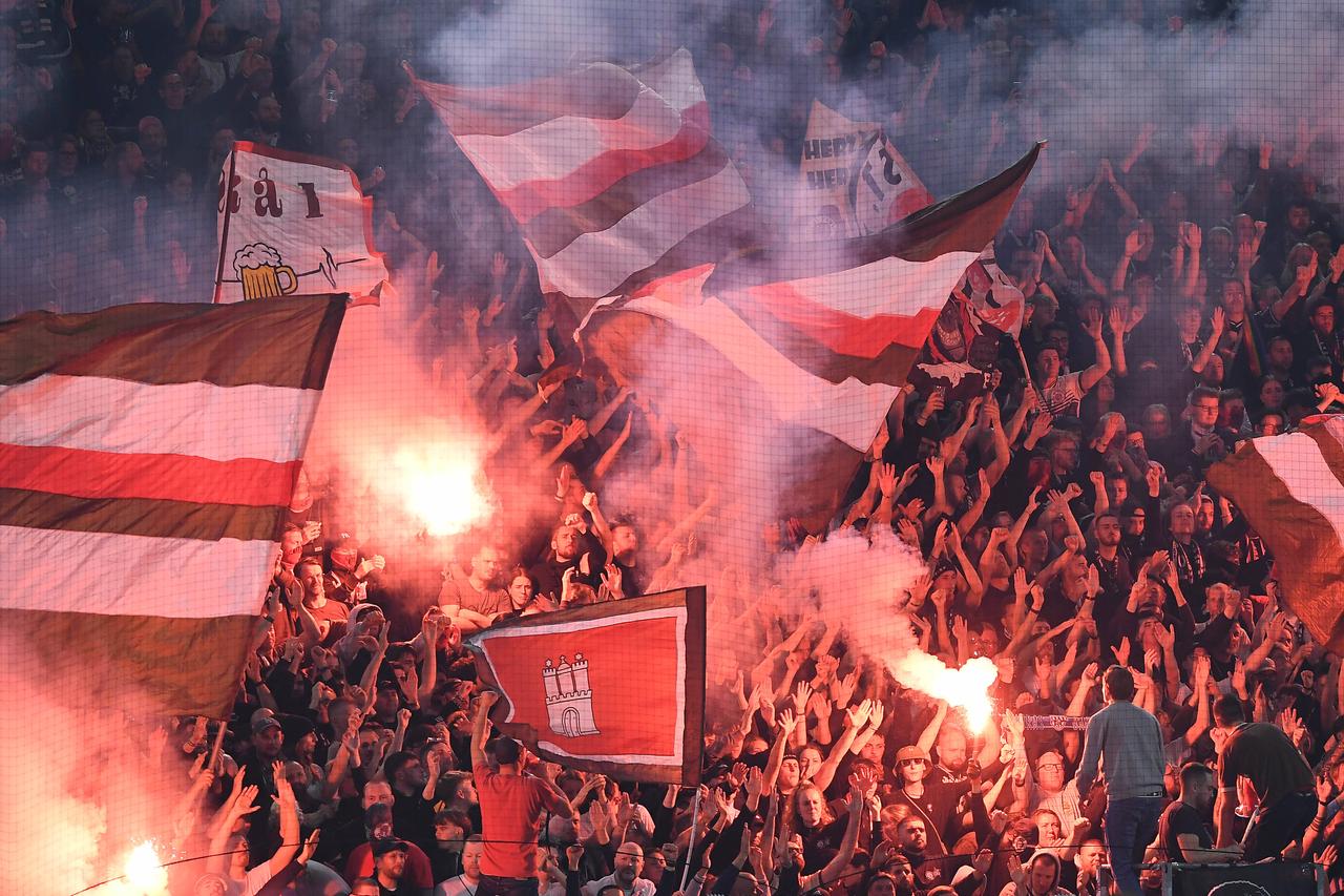 Fans des FC Sankt Pauli brennen auf einer voll besetzten Tribüne rot rauchende Bengalos ab. 