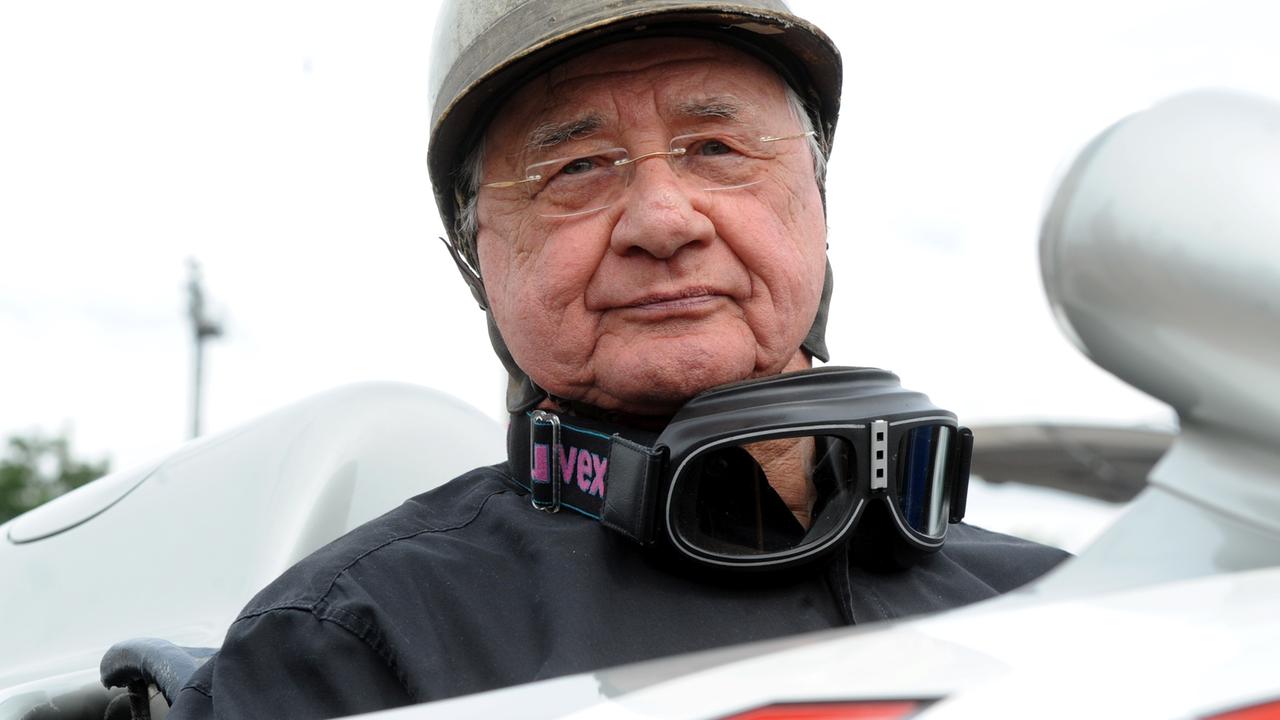Der ehemalige Rennfahrer Hans Herrmann sitzt in einem Rennwagen. 