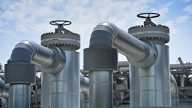 Silberne Industrie-Rohrleitungen mit Ventilen und gebogenen Verbindungsstücken vor einem bewölkten Himmel