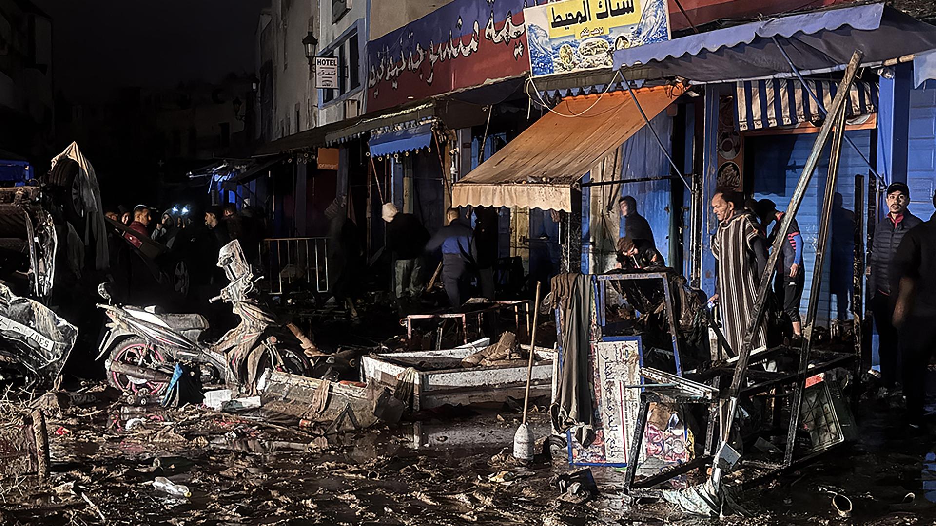 Menschen gehen an Trümmern vorbei, Matsch und Geröll bedecken die Straße. 