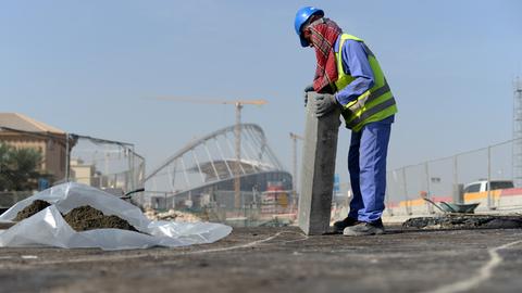 Ein Gastarbeiter bringt an einer Straße vor dem Khalifa-Stadion in der katarischen Hauptstadt Doha einen Bordstein an. 