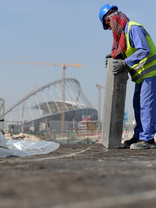 Ein Gastarbeiter bringt an einer Straße vor dem Khalifa-Stadion in der katarischen Hauptstadt Doha einen Bordstein an. 
