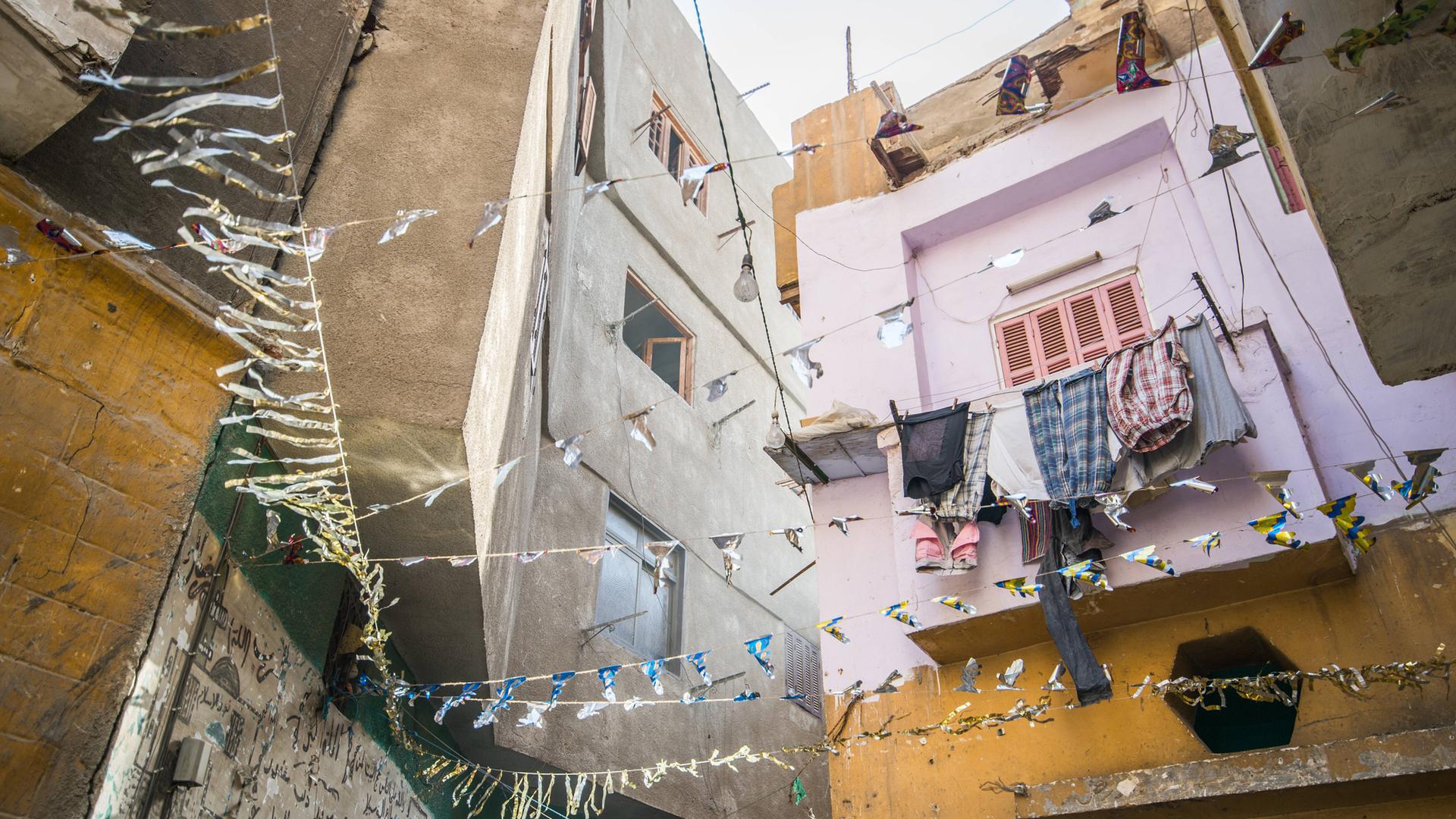Häuserzeile mit hängender Wäsche und Girlanden in einer sonnenbeschienen Gasse in Kairo