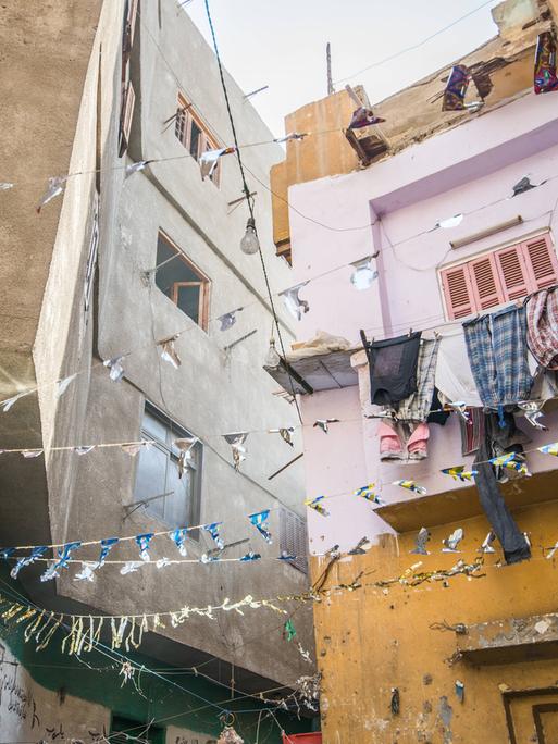 Häuserzeile mit hängender Wäsche und Girlanden in einer sonnenbeschienen Gasse in Kairo