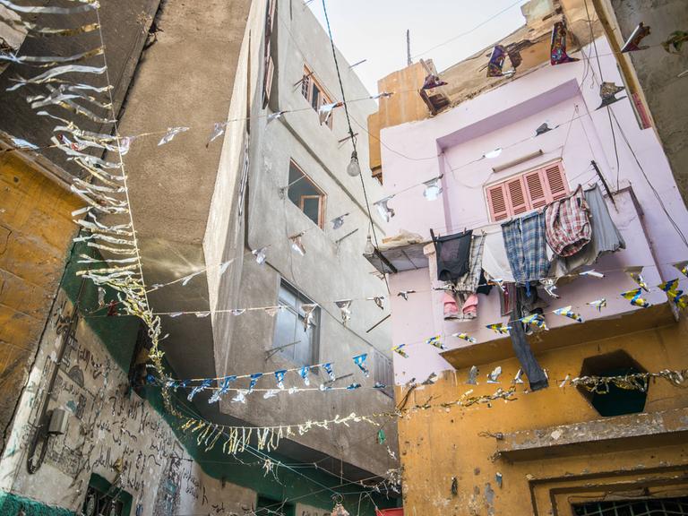 Häuserzeile mit hängender Wäsche und Girlanden in einer sonnenbeschienen Gasse in Kairo