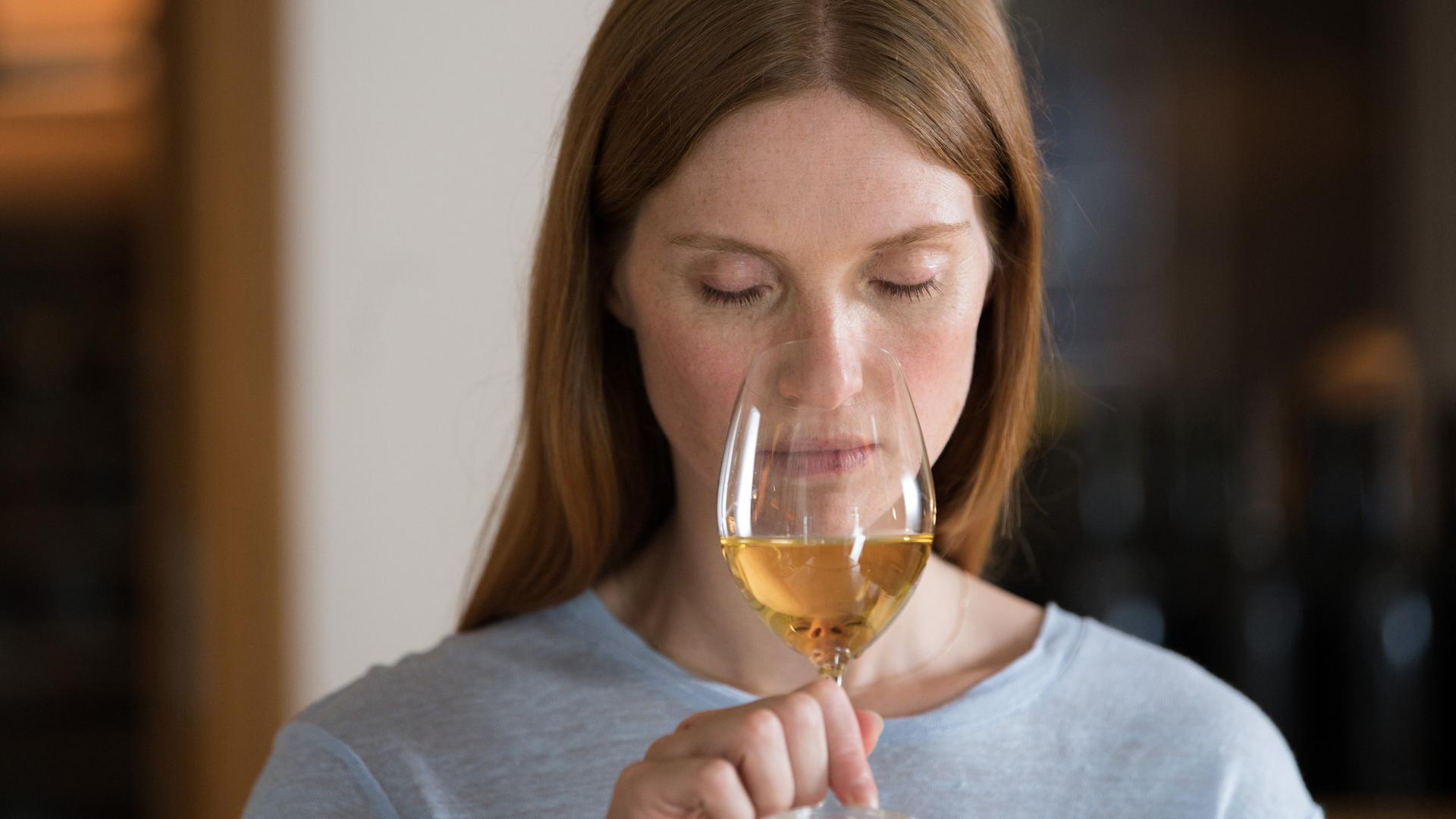 Eine Frau riecht mit geschlossenen Augen an einem Glas Weisswein