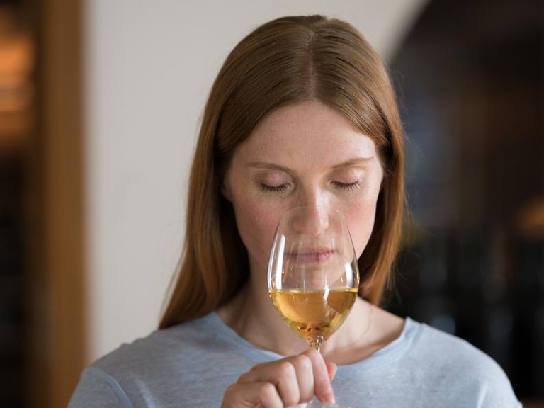Eine Frau riecht mit geschlossenen Augen an einem Glas Weisswein