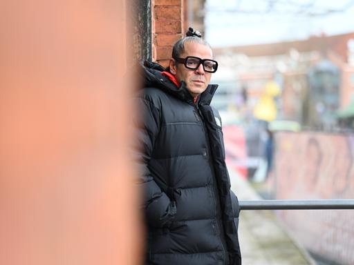 Luigi Toscano lehnt an einer Wand und schaut ernst in die Kamera.