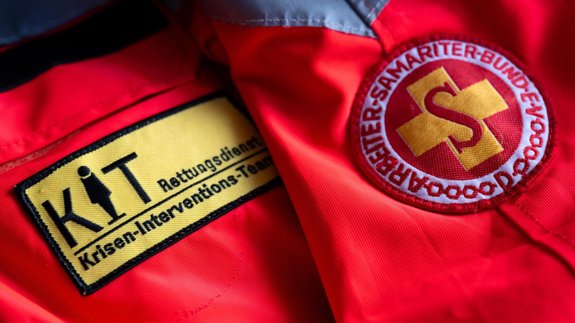 Das Logo vom Münchner Kriseninterventionsteam (KIT, l) und vom Arbeiter-Samariter-Bund (ASB) sind auf einer Uniform zu sehen. 