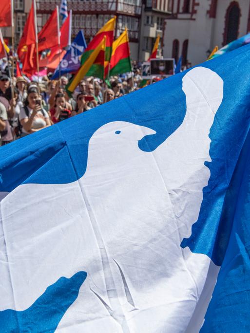 Auf einem Ostermarsch mit zahlreichen Teilnehmern ist eine blaue Fahne mit einer weißenn Friedenstaube zu sehen. 